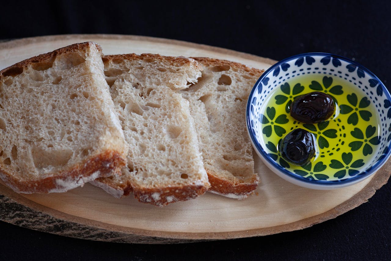 Slices of rustic bread with a dish of olive oil and olives on a wooden board.